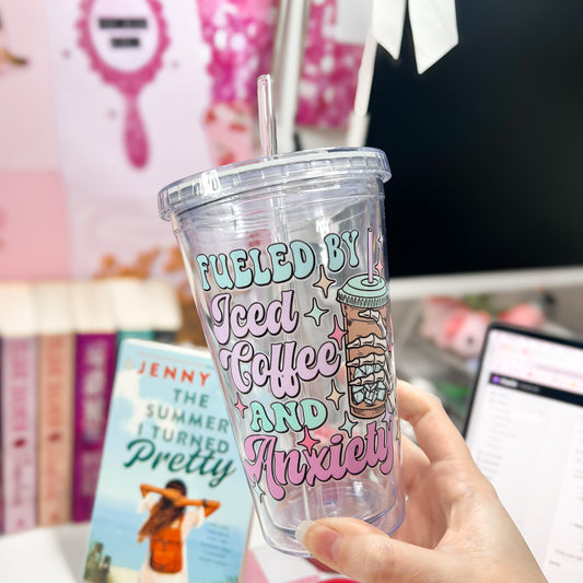 Clear tumbler with colorful text held by a hand, with books and a laptop in the background.